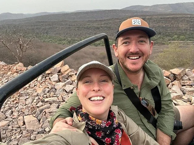 Smiling couple sitting in a safari vehicle overlooking a vast rocky landscape